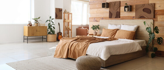 Interior of stylish bedroom with comfortable bed, pouf and houseplants