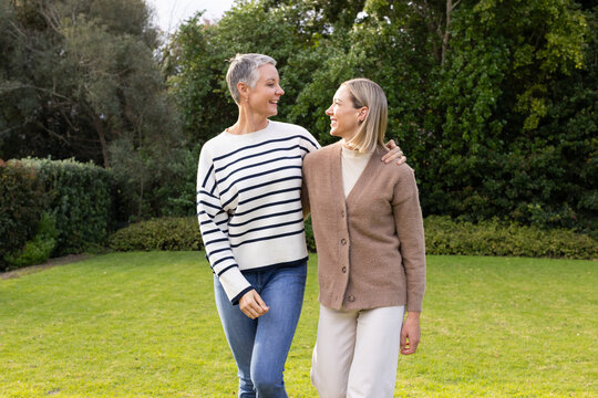 Mother and daughter walking arm in arm across private garden lawn sharing warm smiles