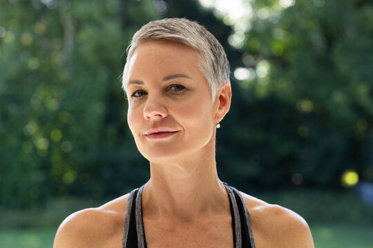 Mature woman sporting pixie haircut and pearl earrings wearing athletic tank posing in garden