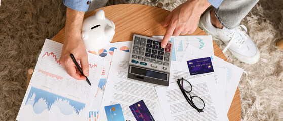 Young man in debt using calculator at home, top view