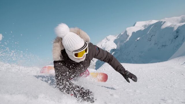 SLOW MOTION, CLOSE UP: Female snowboarder tumbles into soft snow on a sunny alpine slope as she tries to learn to carve on a snowboard. Snow flies toward the camera while she crashes with a smile.