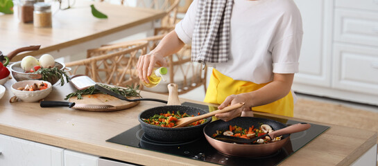 Young housewife pouring oil into fried vegetables in kitchen