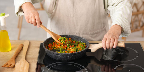 Senior woman frying vegetables in kitchen