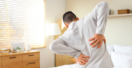 Young man in pajamas suffering from back pain at home