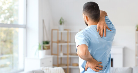 Fototapeta premium Young man suffering from back pain at home
