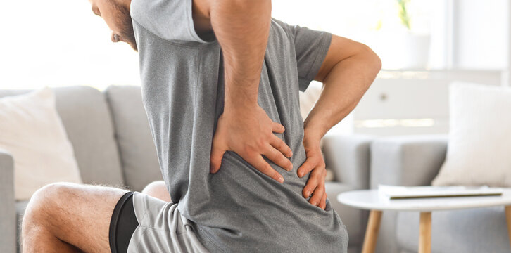 Sporty young man suffering from back pain on fitball at home