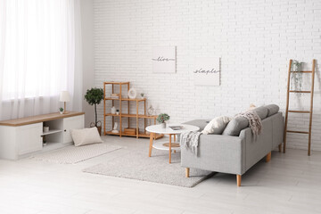 Interior of light living room with comfortable sofa, bench, coffee table and shelving unit