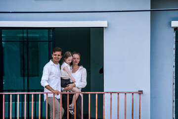 Obraz premium A happy family of three shares a loving moment on the balcony of their modern home. The daughter kisses her mother's cheek, showcasing joy, affection, and peaceful family life.