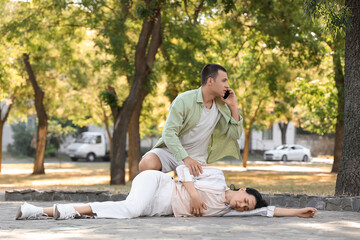 Young man calling ambulance for unconscious woman having heart attack in park © Pixel-Shot