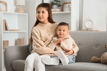 Teenage girl hugging her little brother on sofa at home