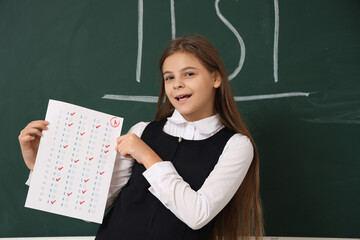 Happy schoolgirl with results of test near blackboard in classroom