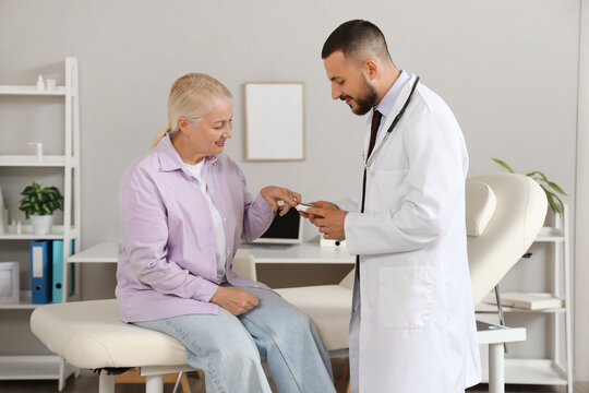Male doctor with mature woman using glucometer in clinic
