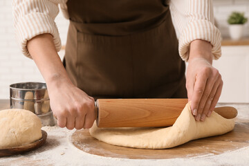 Woman rolling out fresh dough in kitchen