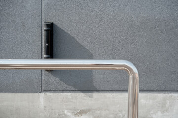 Stainless steel handrail and black sensor on gray wall, modern safety and security detail.
