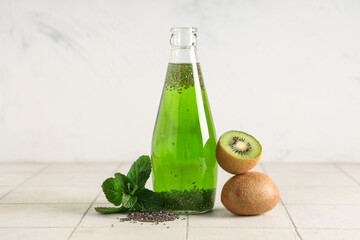 Bottle of lemonade with chia seeds, kiwis and mint on tile table against white grunge background