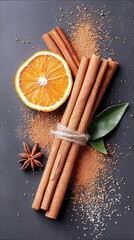 A collection of warm, aromatic spices including cinnamon sticks, a dried orange slice, star anise, and powdered cinnamon are artfully arranged on a dark, textur