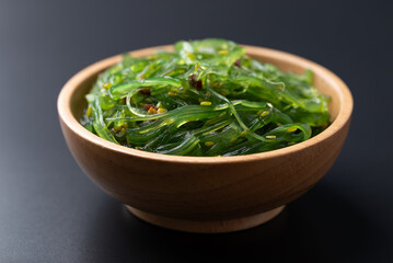 Wakame seaweed salad with sesame seed in a wooden bowl on black background