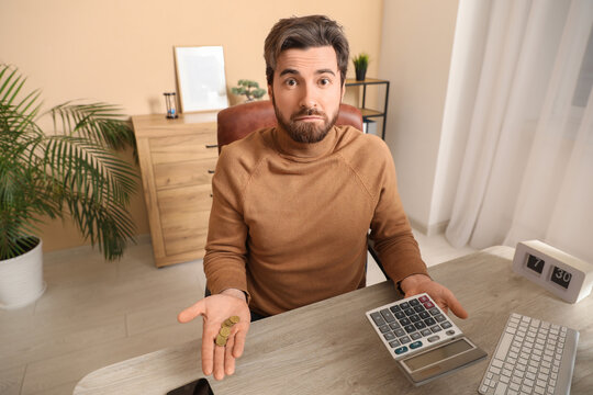 Shocked businessman with calculator at table in office