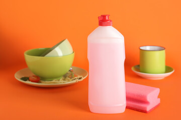 Dirty dishes, pink detergent and sponge on orange background