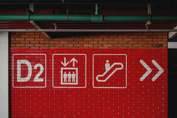 Red brick wall with D2 parking zone signs, elevator and escalator icons, garage interior wayfinding.