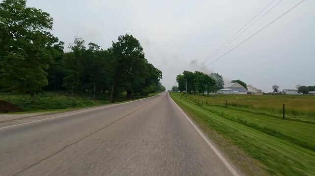 Car point of view traveling on a two lane rural highway in the Midwest, USA. A farm tractor is driving on the side of the road, a common sight in this area. Captured in Springtime near Arthur, IL.