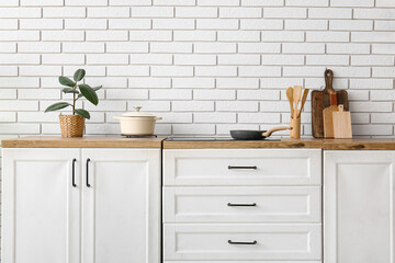 Counters with stove, utensils and plant near white brick wall in kitchen