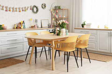 Interior of festive kitchen with tulip flowers, rabbits and Easter painted eggs on tree branches at dining table