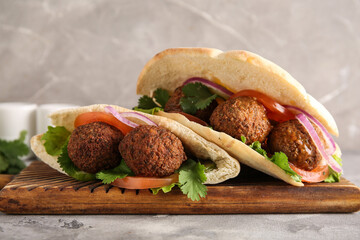 Wooden board of delicious pitas with falafel on grey background