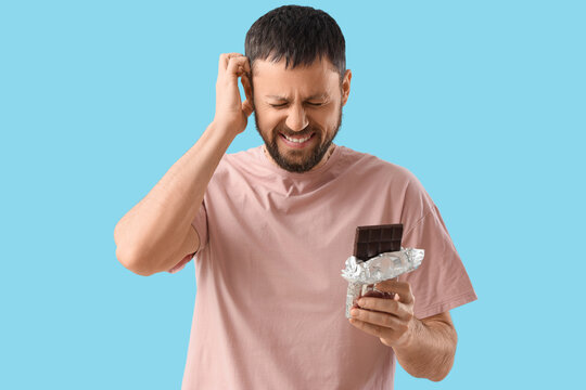 Young man with chocolate bar itching on blue background. Food Allergy Awareness Month
