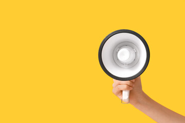 Female hand with megaphone on yellow background