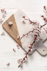 Cutting board with beautiful blooming branch and flowers on white wooden background