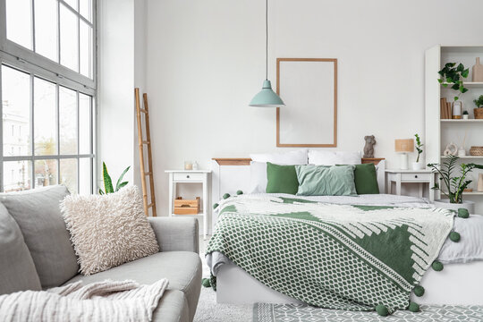 Interior of light bedroom with cozy bed, shelving unit and houseplants