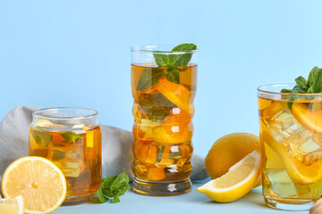 Glasses of lemon ice tea with mint and citrus fruits on blue background