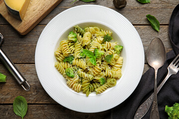 Plate of delicious fusilli pasta with broccoli and basil leaves on wooden background