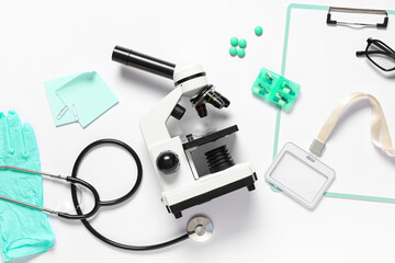 Modern microscope with stethoscope, clipboard and medicine on white background