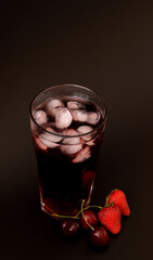 Tall glass of strawberry and cherry berry juice with ice on black background.