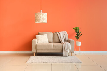 Comfortable beige sofa and houseplant near orange wall in interior of living room