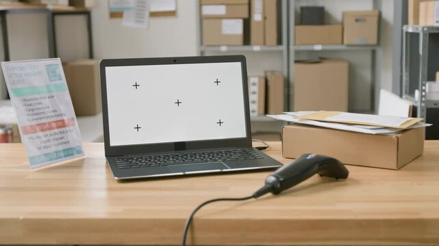 No people panning shot of laptop computer with empty screen, barcode scanner, package, envelopes, information leaflet at logistics company. Boxes stacked on racks, ready for shipping