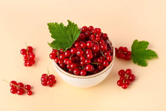 Bowl with ripe red currant and green leaves on beige background, closeup