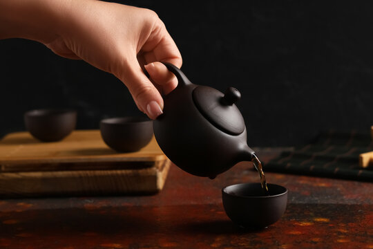 Female hand pouring tea into black cup on grunge table, closeup - Powered by Adobe