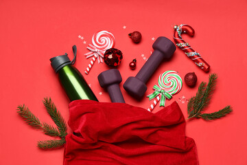 Santa bag with dumbbells, water bottle and Christmas decor on red background