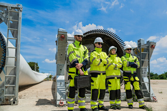 engineers in hard hats and high-visibility jackets inspect a massive piece of industrial equipment on a construction site, collaborating to ensure safety and proper assembly. - Powered by Adobe