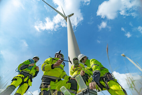 Engineers at a wind farm use a drone for inspection near a wind turbine. The image highlights the use of technology in renewable energy, wind power projects, and modern energy solutions.