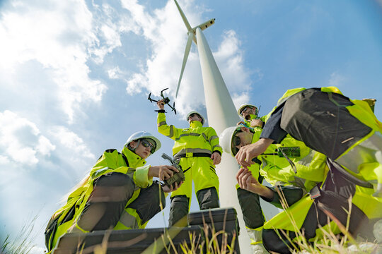 Engineers at a wind farm use a drone for inspection near a wind turbine. The image highlights the use of technology in renewable energy, wind power projects, and modern energy solutions.