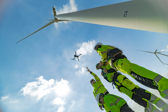 engineers conducting an aerial inspection of a wind turbine using a drone. The scene highlights modern technology&rsquo;s role in renewable energy maintenance, showcasing collaboration and innovation.