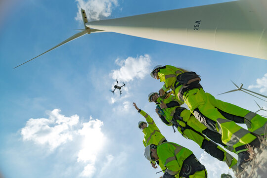 engineers conducting an aerial inspection of a wind turbine using a drone. The scene highlights modern technology’s role in renewable energy maintenance, showcasing collaboration and innovation. - Powered by Adobe