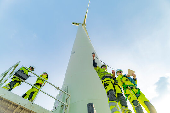 A team of engineers inspects and maintains a large wind turbine at a renewable energy wind farm. Green technology and sustainable practices are at the forefront of renewable energy development.