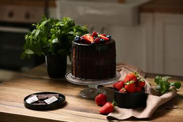 Tasty chocolate cake with fresh berries and mint on table in kitchen