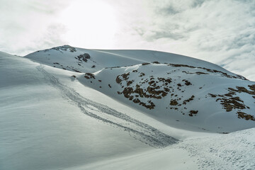 view of a snowy hillside on a winter day with the marks of walkers' footprints and clouds in the blue sky.
