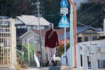 秋の朝の住宅街で歩くシニア男性の姿
